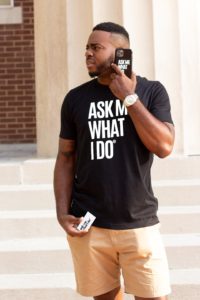 man talking on a phone with 'ask me what I do' on his t-shirt, phone and business card.