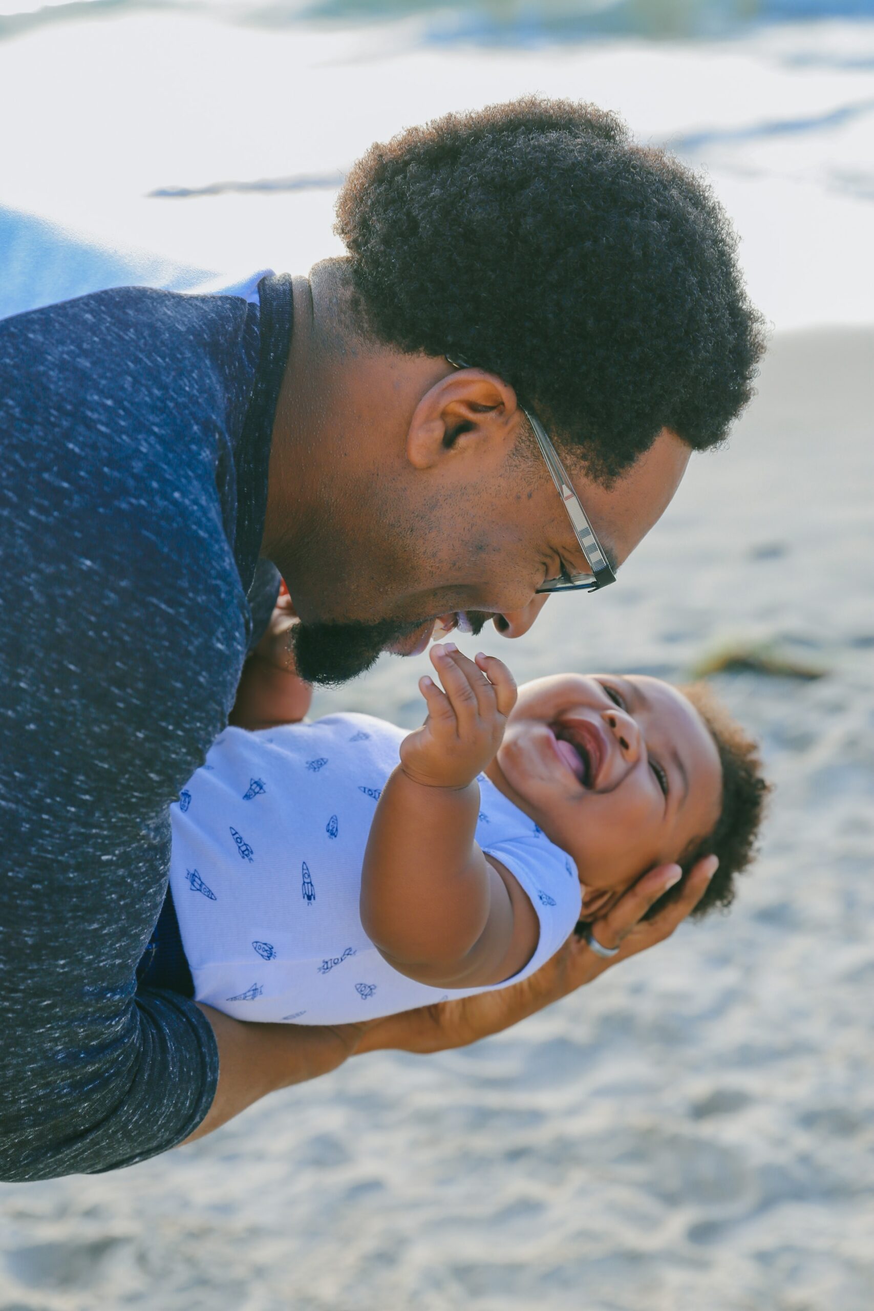 man on the beach laughing while playing with a baby as a boss